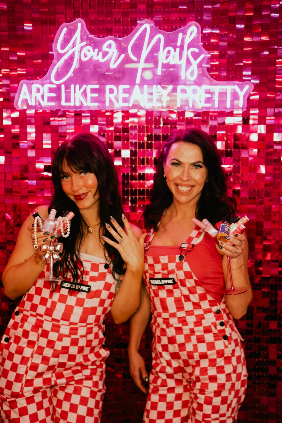 Mandi and Dakota, mother-daughter co-owners of Pinkies Beauty Bar, in front of the pink sequin wall